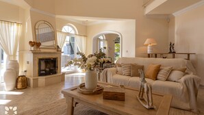 A spacious living room with a fireplace, a sofa, a coffee table, and a view of the outdoors through large windows. - Villa Marcela by Abahana Villas (Teulada)
