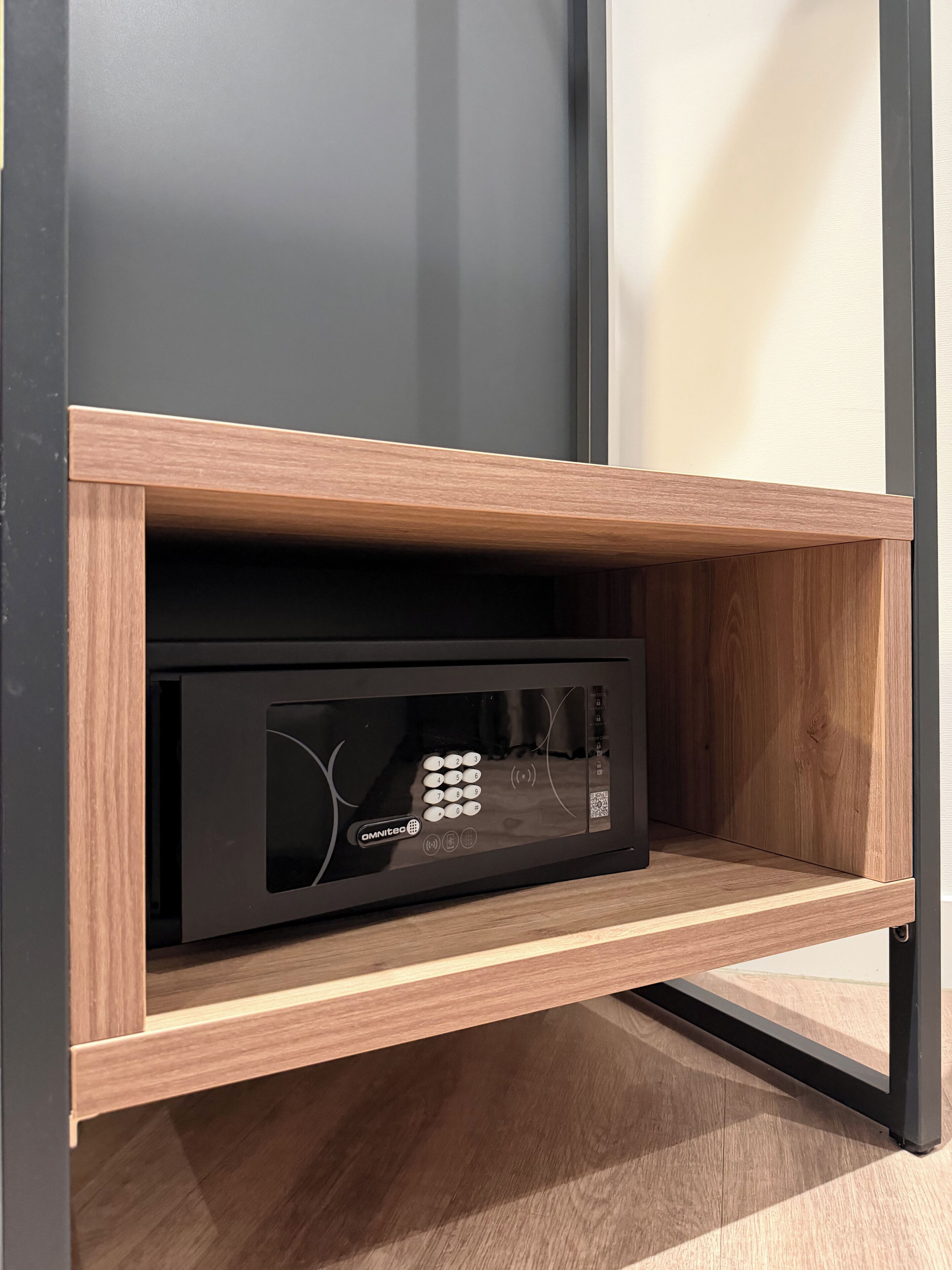 A black electronic device with a keypad and QR code, placed in a wooden shelf with metal legs.