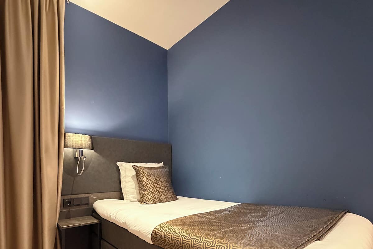 A modern hotel room with a large bed, a bedside table with a lamp, and a curtain.