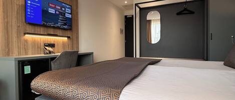 A modern hotel room with a bed, a desk, a television mounted on the wall, and a ceiling fan.