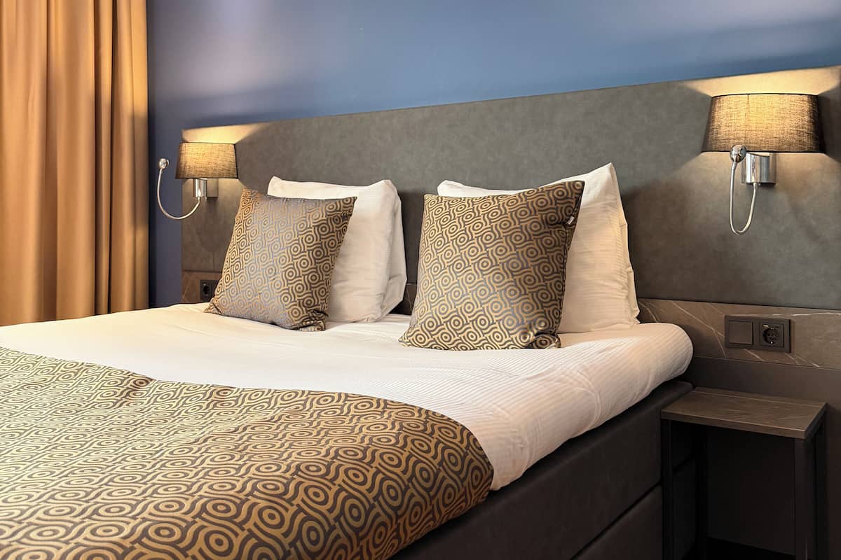 A hotel room with a large bed, two bedside lamps, a headboard, and a nightstand.