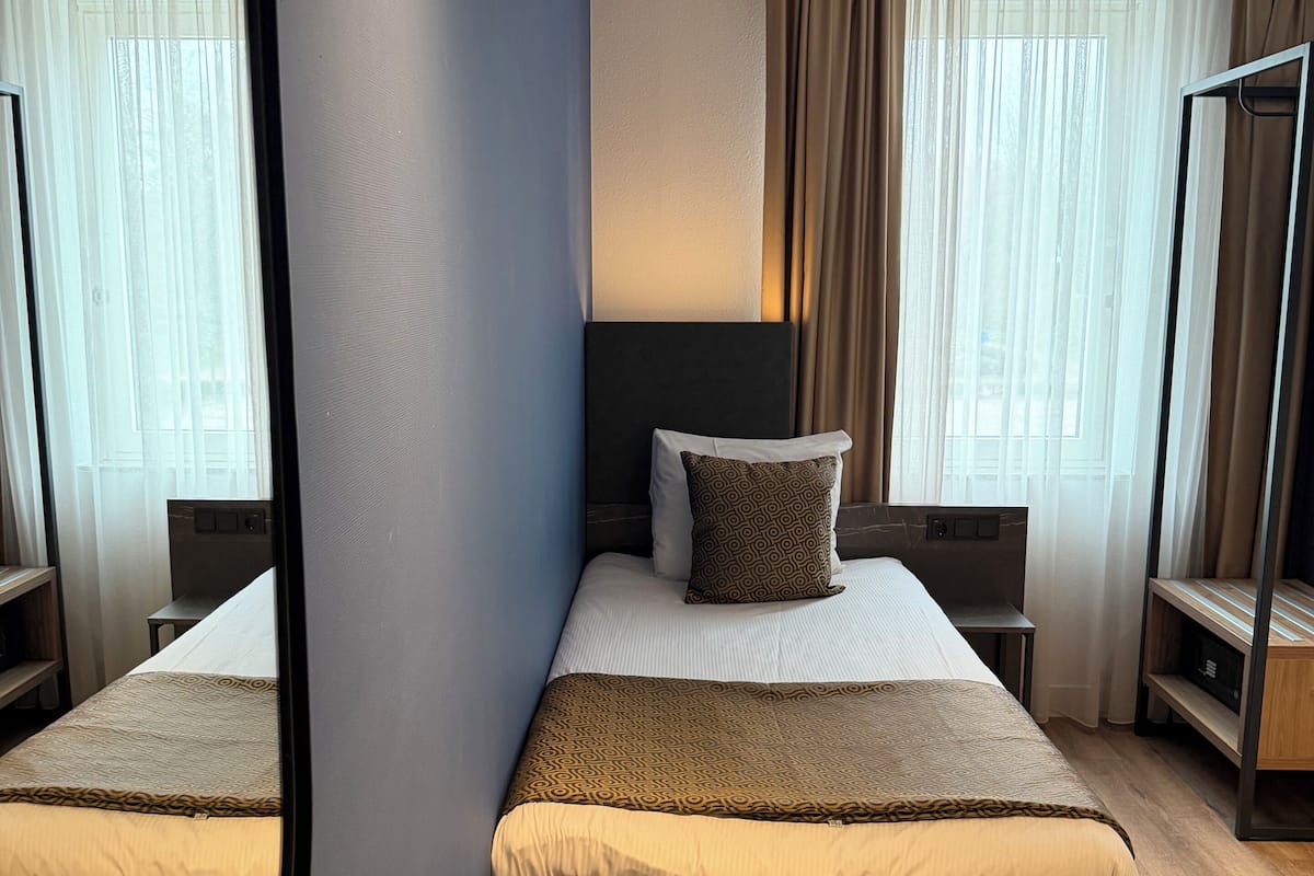 A double bed with a headboard, bedside tables, a mirror, and a view of the outdoors through sheer curtains.