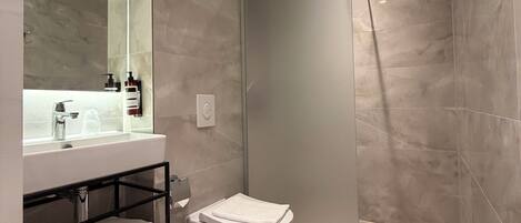 A modern bathroom with a large mirror, a white sink, a toilet, and a shower area.