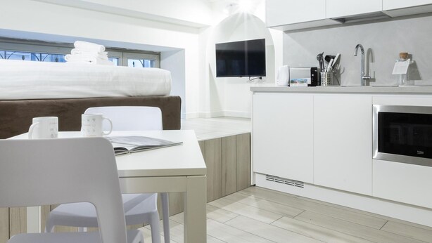 A modern kitchen with white cabinetry, a dining area with a table and chairs, and a view of the outdoors through a window.