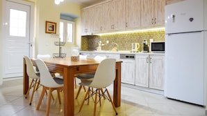 A kitchen with a wooden dining table, four chairs, white cabinets, a white refrigerator, and a patterned backsplash.