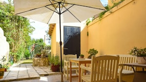 An outdoor patio with a table and chairs, a large umbrella, and potted plants.