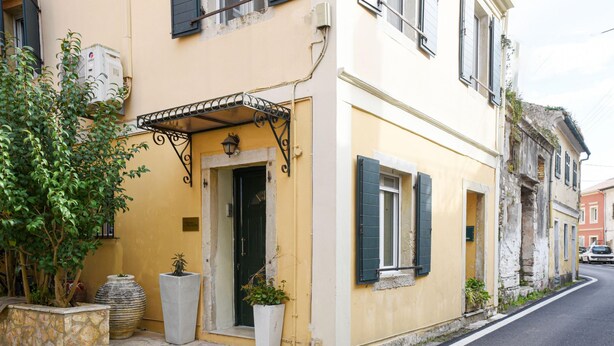 A yellow building with a stone entrance, potted plants, and a street view.