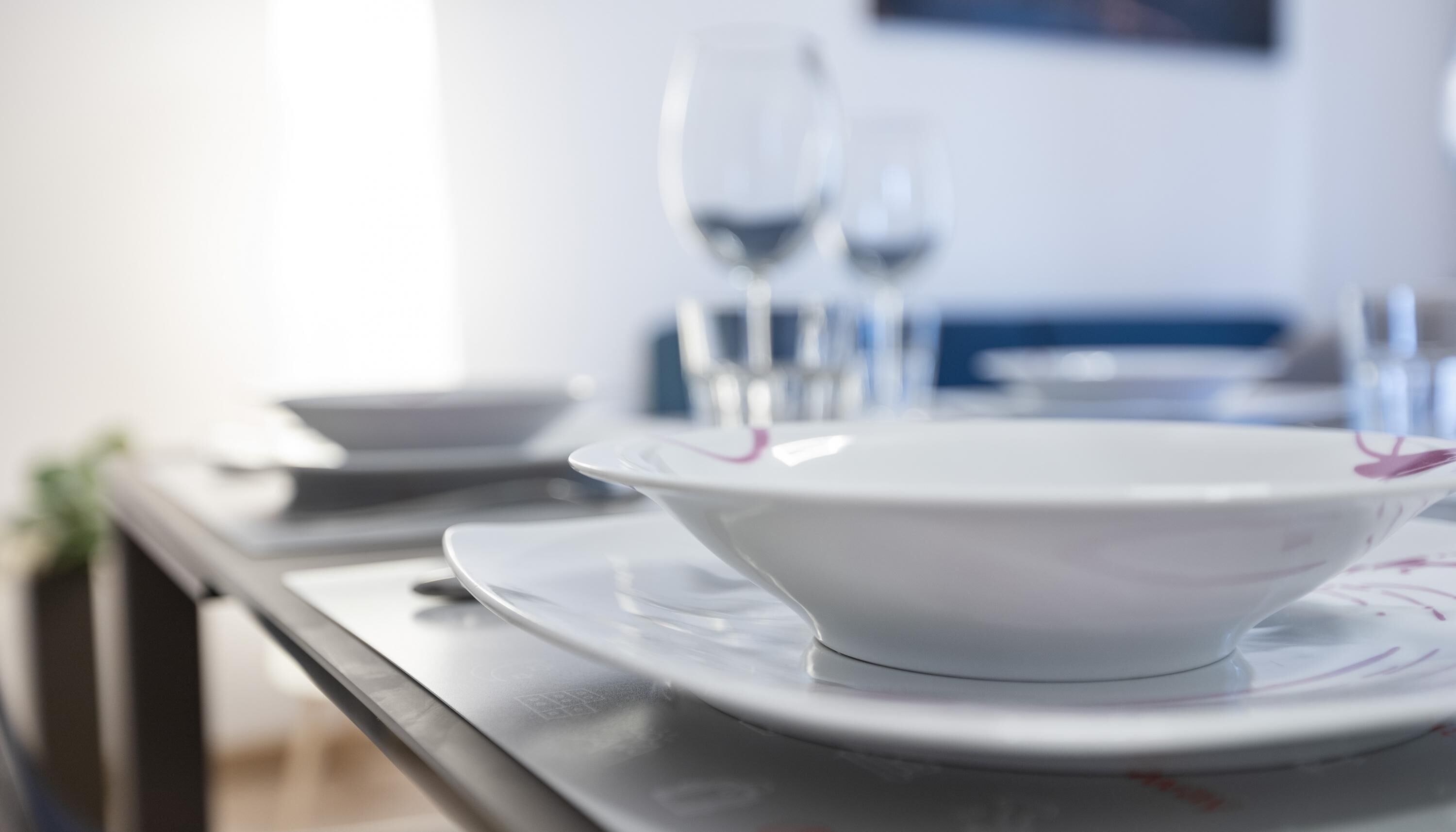 Une table à manger avec un saladier et des assiettes blancs, des verres et une télécommande.