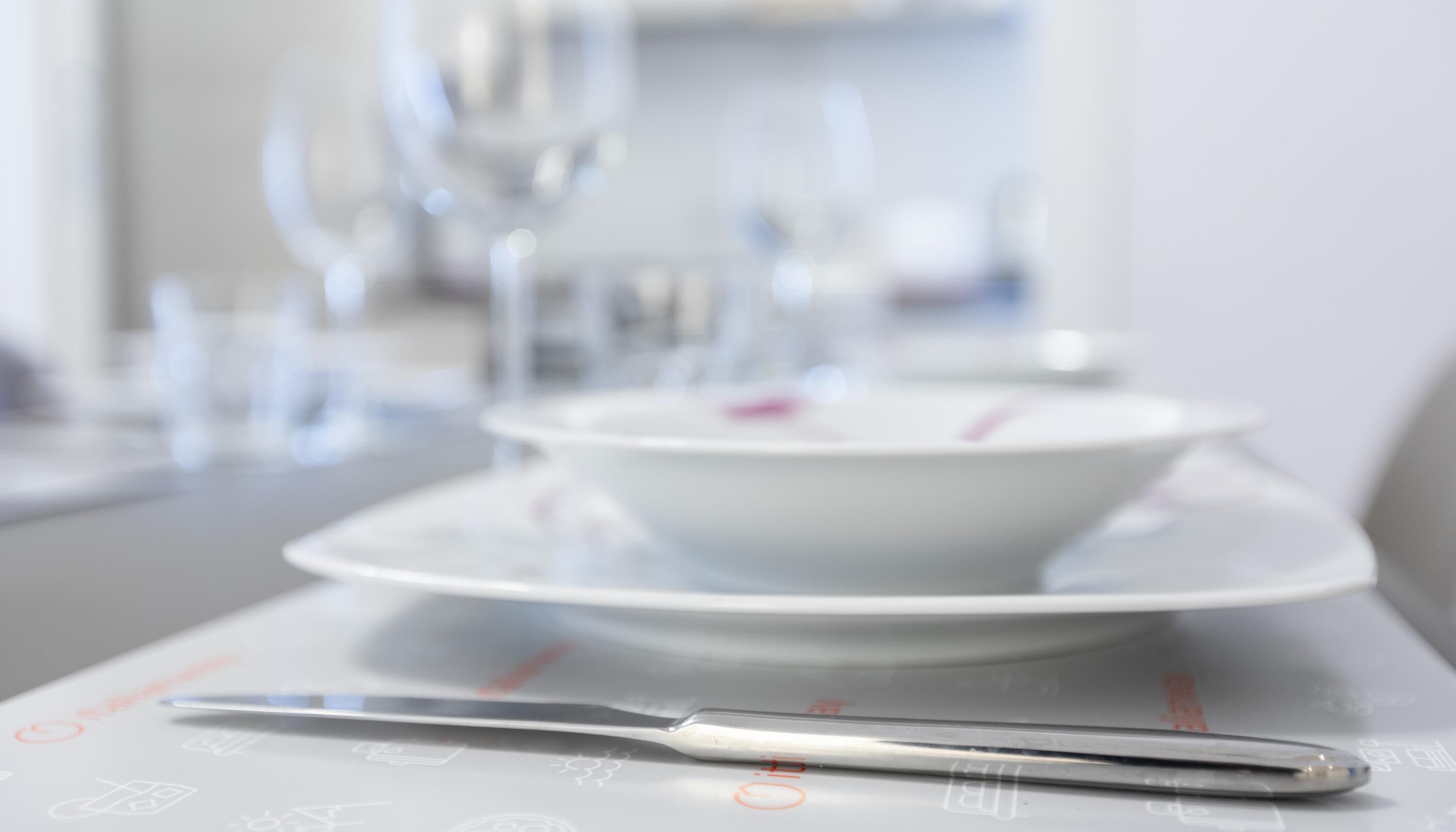 Une table à manger recouverte d’une nappe blanche, avec un bol, une cuillère et un couteau.