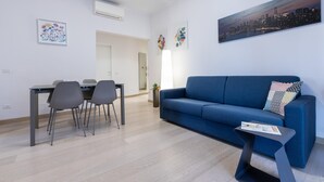 Ein modernes Wohnzimmer mit einem blauen Sofa, einem Esstisch mit Stühlen und Kunstwerken an den Wänden.
