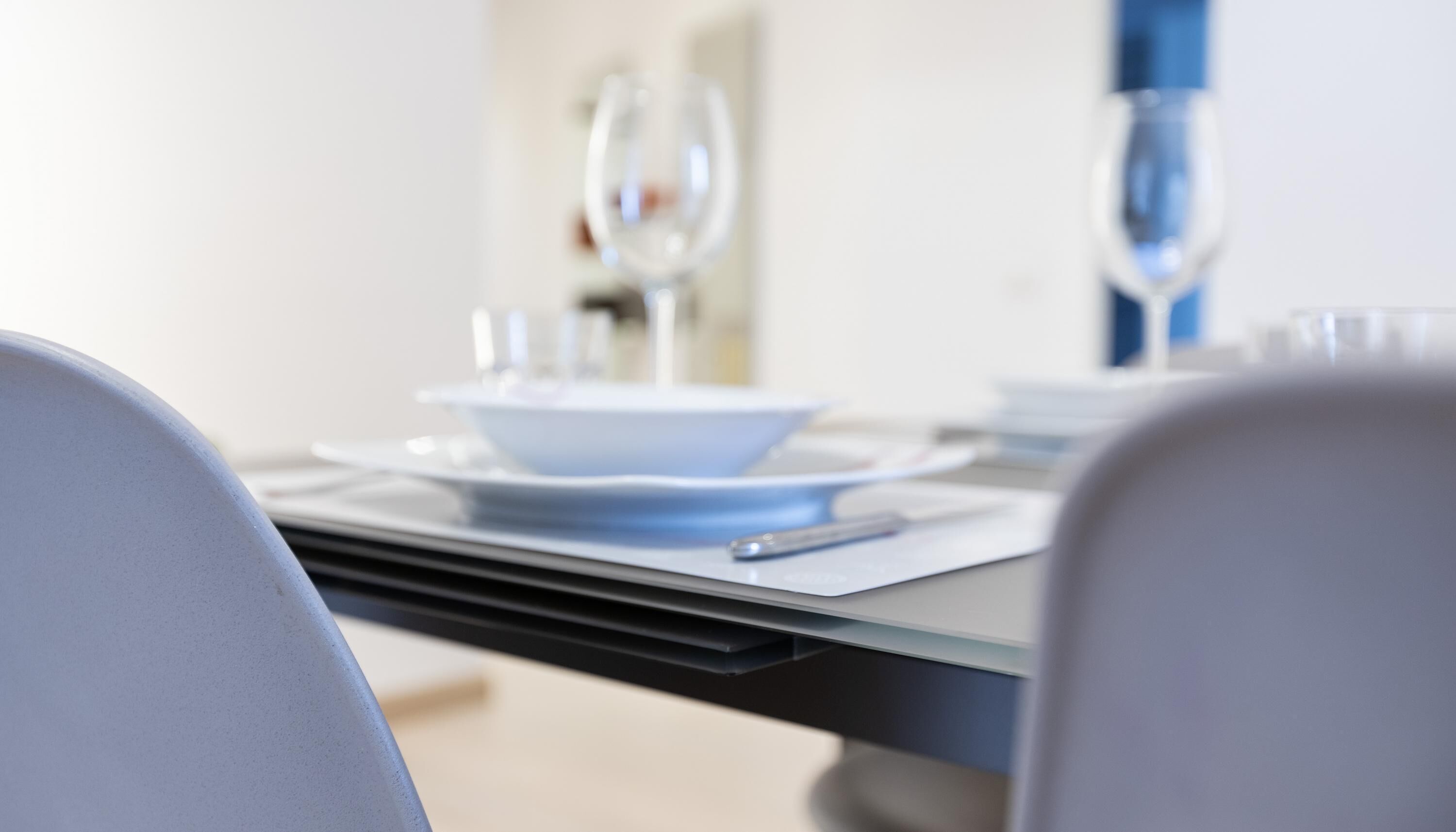 A dining table set with plates, cutlery, and glasses, with a chair in the foreground.