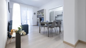 Ein modernes Wohnzimmer mit Essbereich, einer Küche und einem großen Fenster mit transparenten Vorhängen.