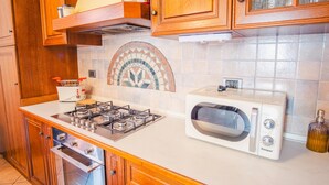A kitchen with wooden cabinets, a gas stove, a microwave, and a tiled backsplash. - Al Bivio Peschiera - Italian Homing (Peschiera del Garda)