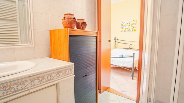 A bathroom with a sink, toilet, and decorative tiles. There is a door leading to a bedroom with a bed and a wall with a circular pattern. - Al Bivio Peschiera - Italian Homing (Peschiera del Garda)