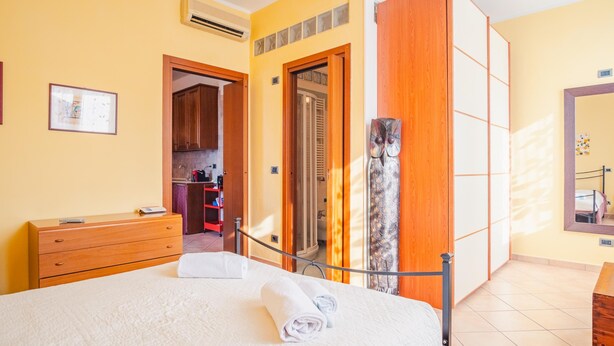 A hotel room with a bed, a wooden dresser, a bathroom visible through an open door, and a large mirror on the wall. - Al Bivio Peschiera - Italian Homing (Peschiera del Garda)