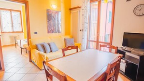 A bright living area with a sofa, a dining table, and a TV. - Al Bivio Peschiera - Italian Homing (Peschiera del Garda)