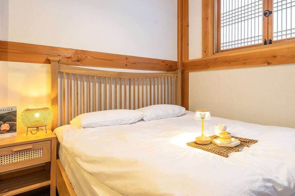 Ein ordentlich gemachtes Bett mit weißen Leinen, eine Nachttischlampe und ein Tablett mit Tasse und Gebäck auf dem Nachttisch.