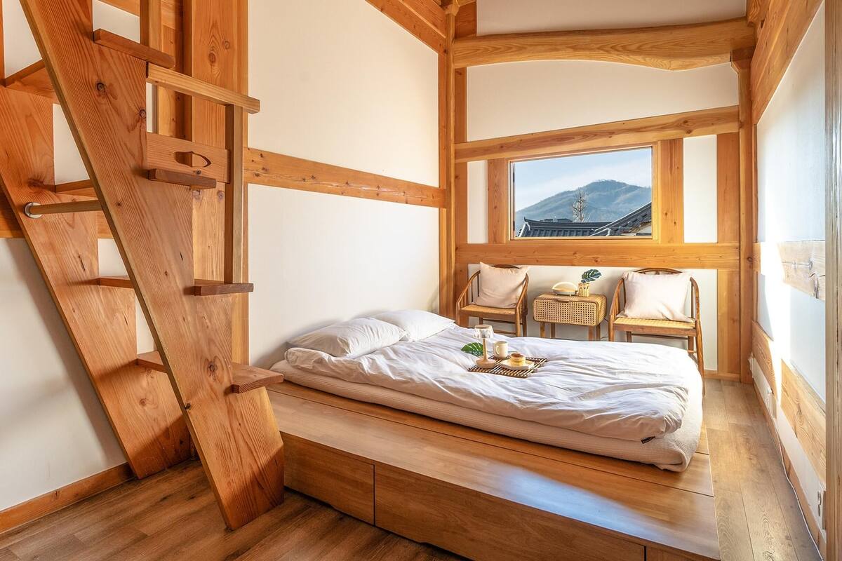 Ein Schlafzimmer mit einer Holzleiter, einem Bett, einem Fenster mit Bergblick und einem kleinen Tisch mit einer Pflanze.