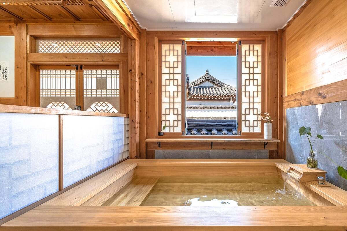 Ein traditionelles japanisches Onsen mit Holzbauten, Blick auf einen Tempel durch ein Fenster und einer kleinen Pflanze am Rand.