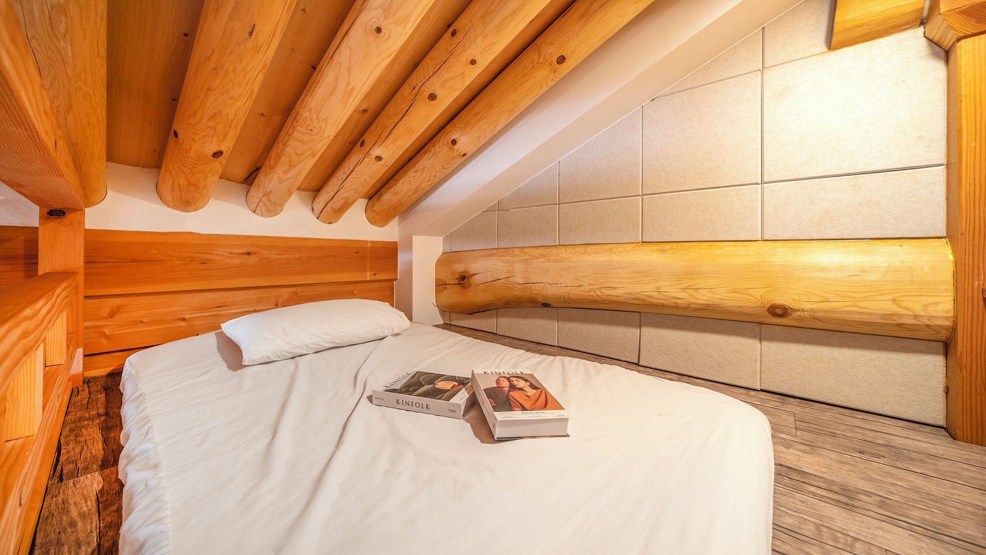 Une chambre à coucher avec une tête de lit en bois, un lit recouvert de draps blancs et deux livres posés sur le lit.