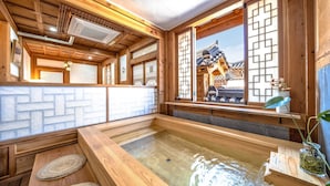 Perinteinen japanilaistyylinen huone, jossa on tatamimatto, puinen sisustus ja näkymä perinteiselle rakennukselle shoji-seinän läpi.