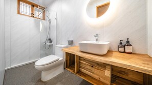 Un baño moderno con inodoro blanco, ducha con cerramiento de vidrio, tocador de madera con lavamanos y dos botellas de loción corporal Himalayan Herb.