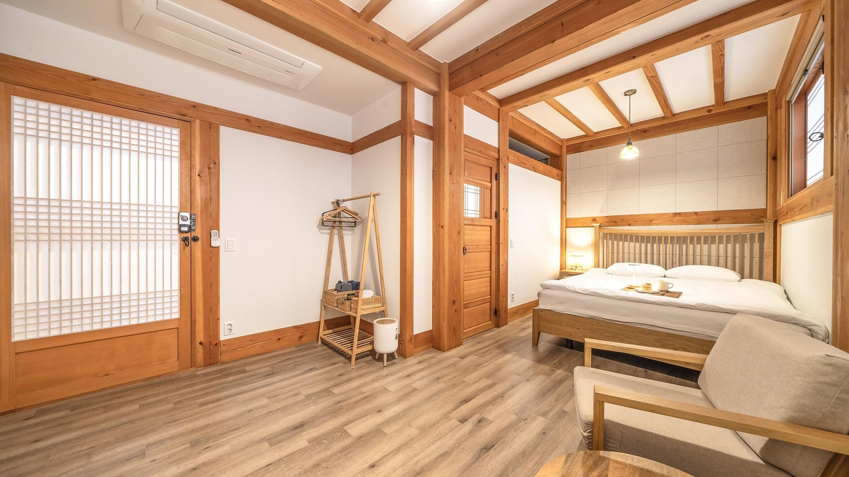 A traditional Japanese-style room with a wooden floor, a bed with a headboard, a hanging light fixture, and a wooden wardrobe.