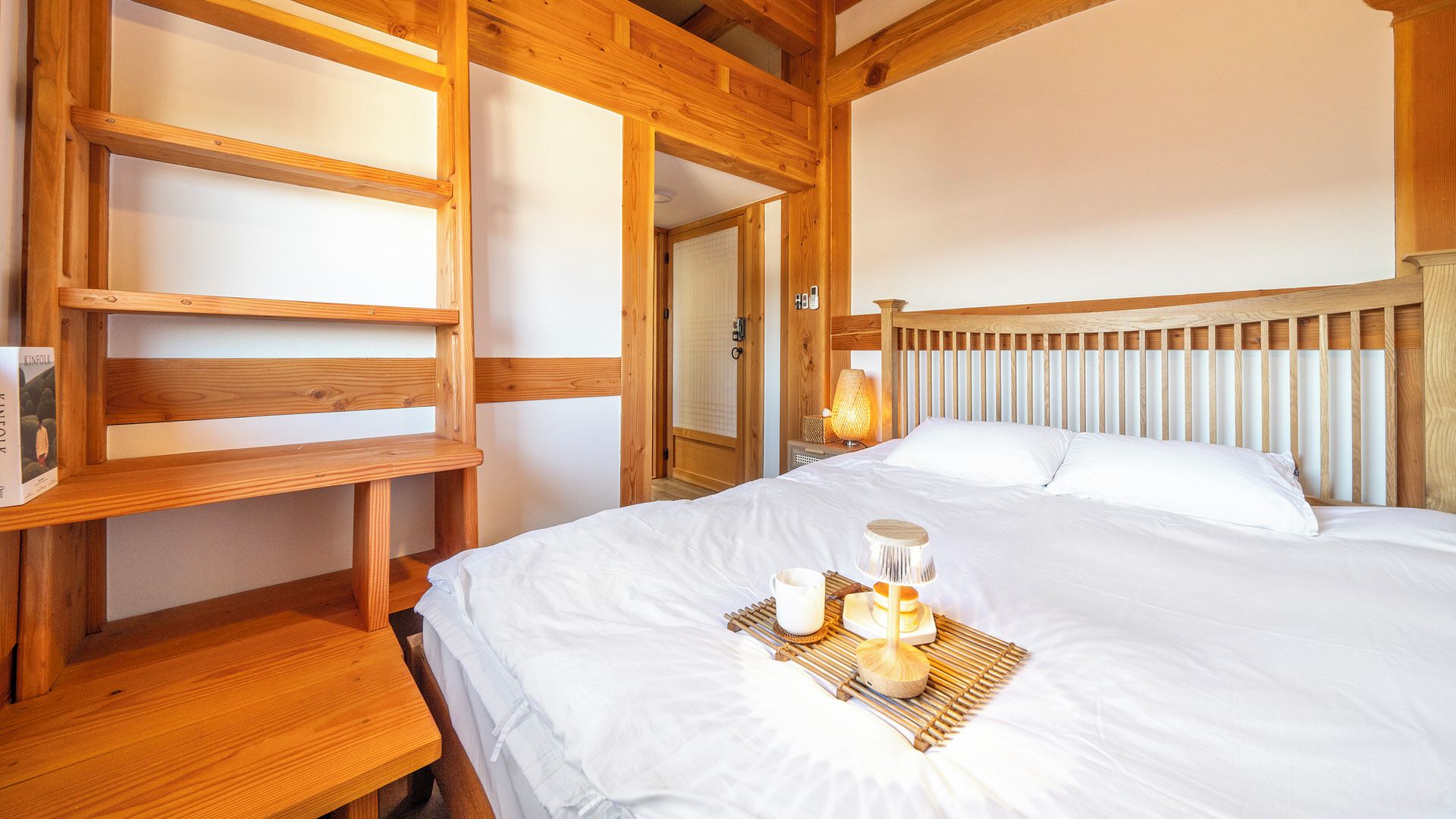 A wooden-framed room with a bed, a bedside table, and a shelf unit.