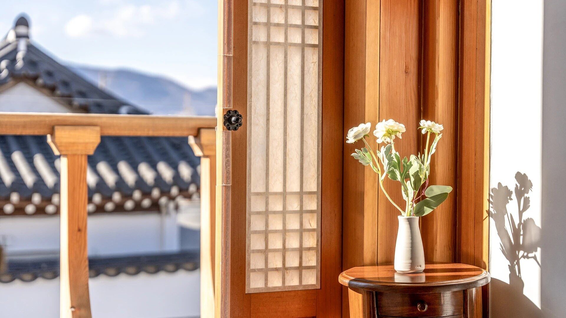 A traditional Japanese room with tatami flooring, a shoji screen, and a wooden balcony with a view of a building and mountains.