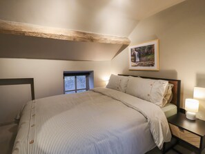 A bedroom with a bed, a nightstand, a lamp, a framed picture on the wall, and a window with a view of greenery. - 8 Oak Cottages (Lancaster)