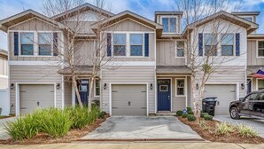 A row of townhouses with attached garages, a driveway, and landscaping. - Pensacola Vacation Rental w/ Community Pool! (Pensacola)