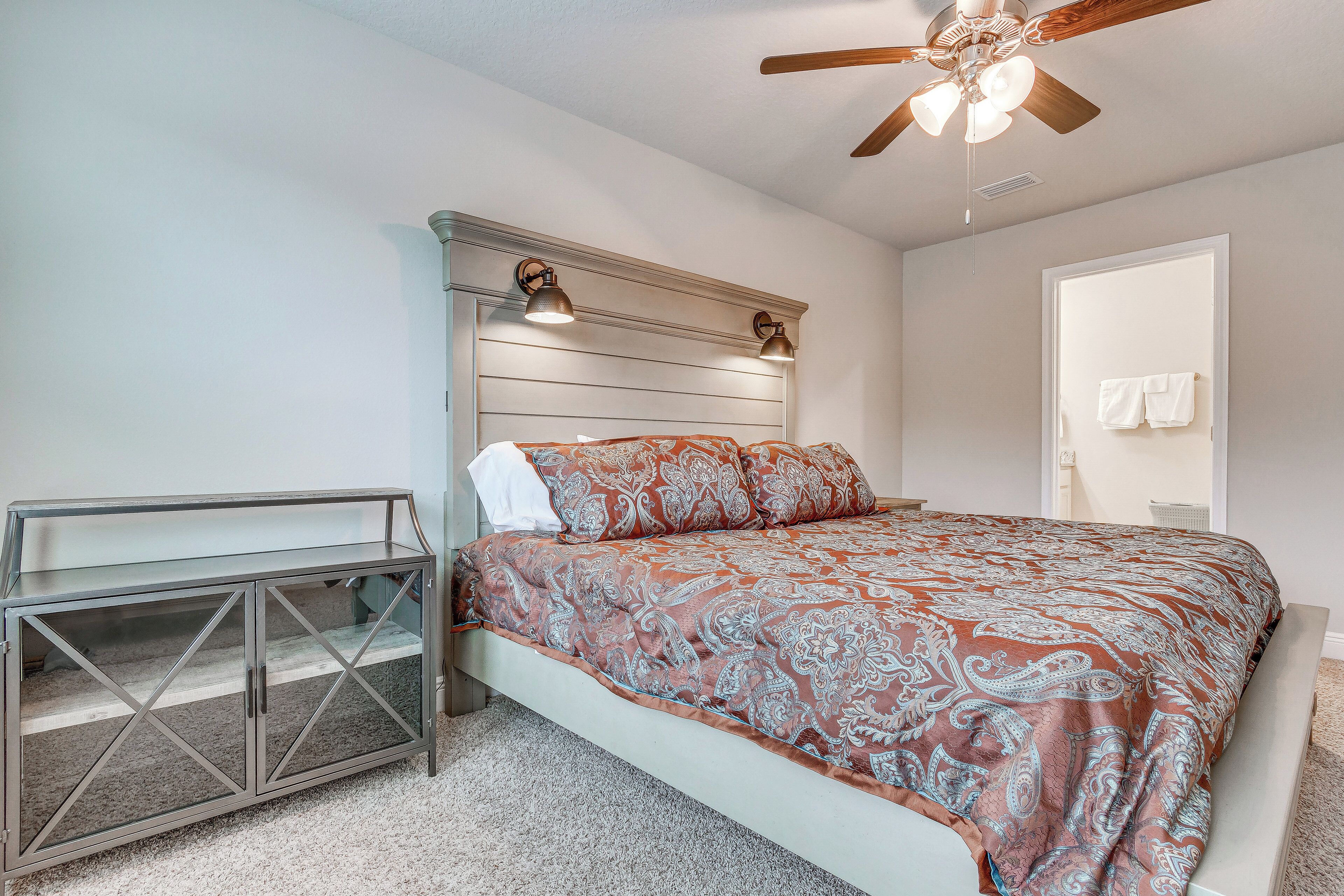 A bedroom with a bed, a glass cabinet, a ceiling fan, and a door with a towel hanging on it.