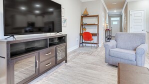 A living room with a flat-screen TV, dark wooden entertainment unit, light grey armchair, and a red chair. - Pensacola Vacation Rental w/ Community Pool! (Pensacola)