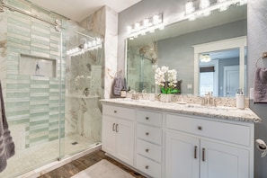 Un baño moderno con cabina de ducha de vidrio, un mueble de tocador espacioso con varios cajones e iluminación integrada en el espejo.