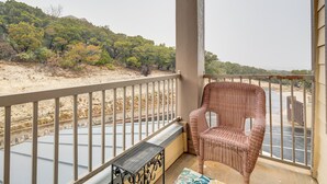 A balcony with a wicker chair, a metal table, and a view of a beach and trees.