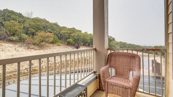 A balcony with a wicker chair, a metal table, and a view of a beach and trees.