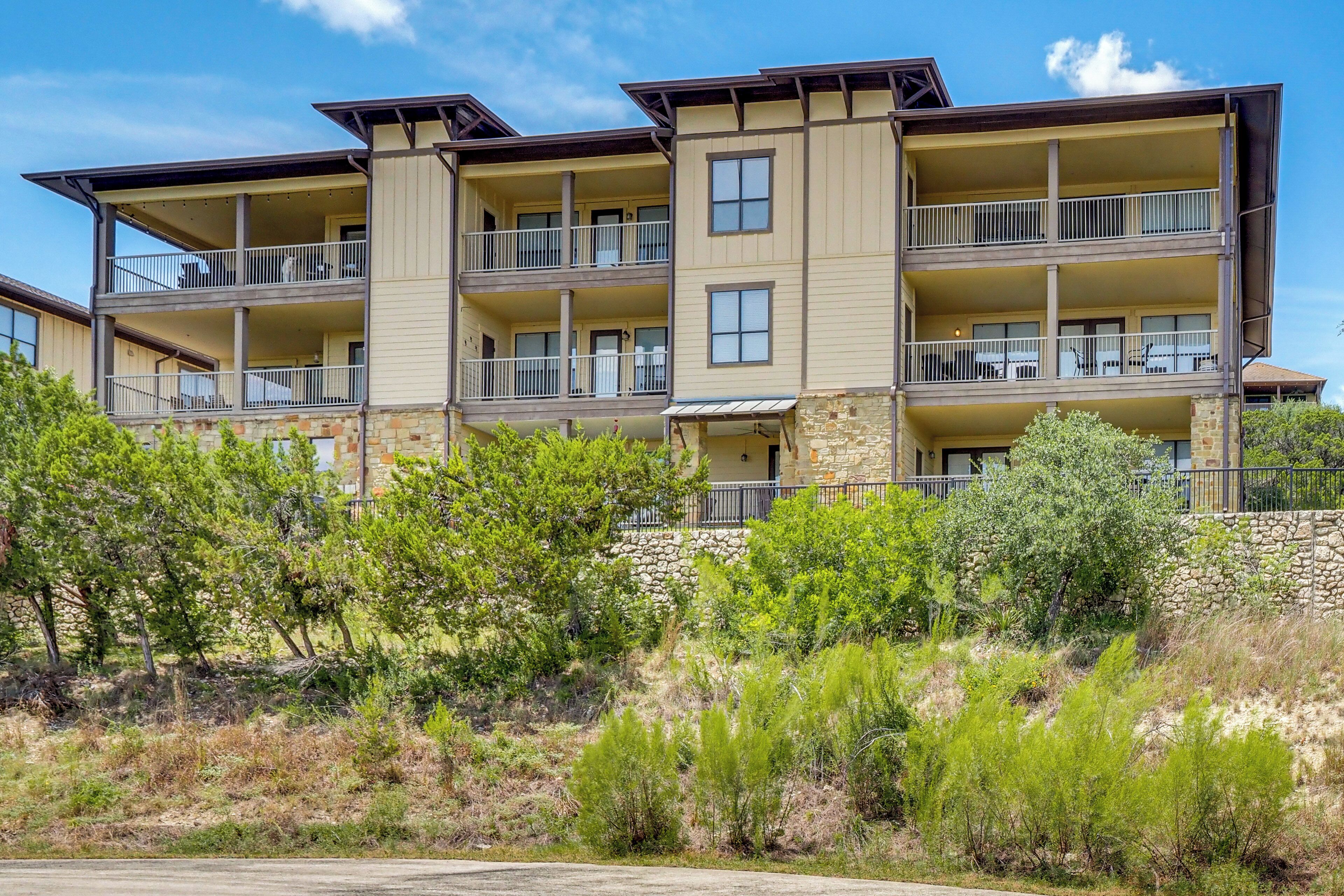 A multi-story hotel with balconies, a stone facade, and a landscaped front yard.