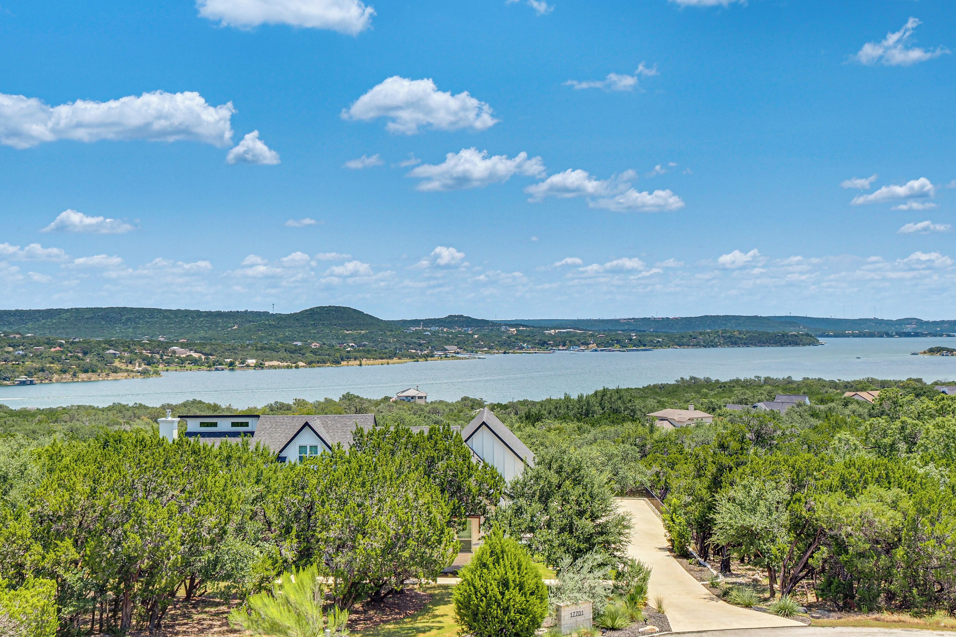 A residential area with a pathway leading to houses, surrounded by greenery and a view of a lake and distant hills.