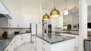 A modern kitchen with white cabinetry, a marble countertop, and gold-toned pendant lights.