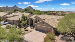 A residential area with multiple houses featuring similar architectural styles, surrounded by natural vegetation and mountains in the background.