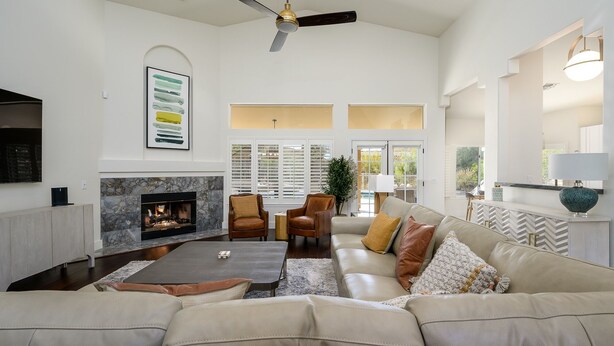 A spacious living room with a fireplace, leather sofa, and a ceiling fan.