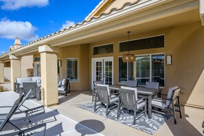 A covered patio area with a dining table and chairs, a hanging light fixture, and a view of the house through large windows. - Casa Pinnacle 3 Bedroom Home by RedAwning (Scottsdale)