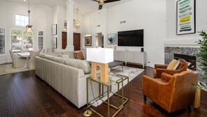 A modern living room with a sectional sofa, a glass coffee table, leather armchairs, a fireplace, and a flat-screen TV.