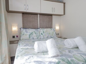 A neatly made bed with a floral bedspread, two white towels, and a headboard with a brown panel.
