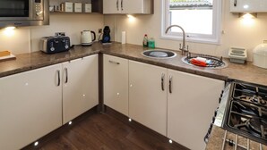 Une cuisine compacte avec des meubles blancs, un four à micro-ondes, un grille-pain, une bouilloire, un évier et une cuisinière.