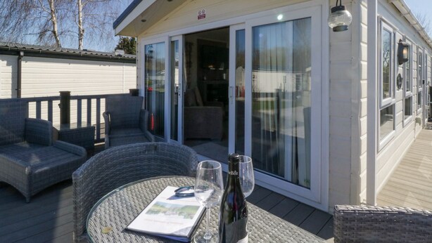 Un espace extérieur aménagé avec des meubles en osier, une bouteille de vin et des verres posés sur une table.
