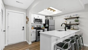 Et moderne køkken med hvide skabe, rustfrie stålapparater, en central ø med barstole og et ovenlys over vasken.