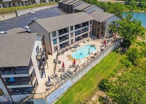 A multi-story hotel with a swimming pool, outdoor seating, and a parking lot. - On Lake Time (Kimberling City)