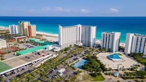 A high-rise hotel with a pool, surrounded by a parking lot and a beach. - Pelican Beach 1911 1 Bedroom Condo (Destin)
