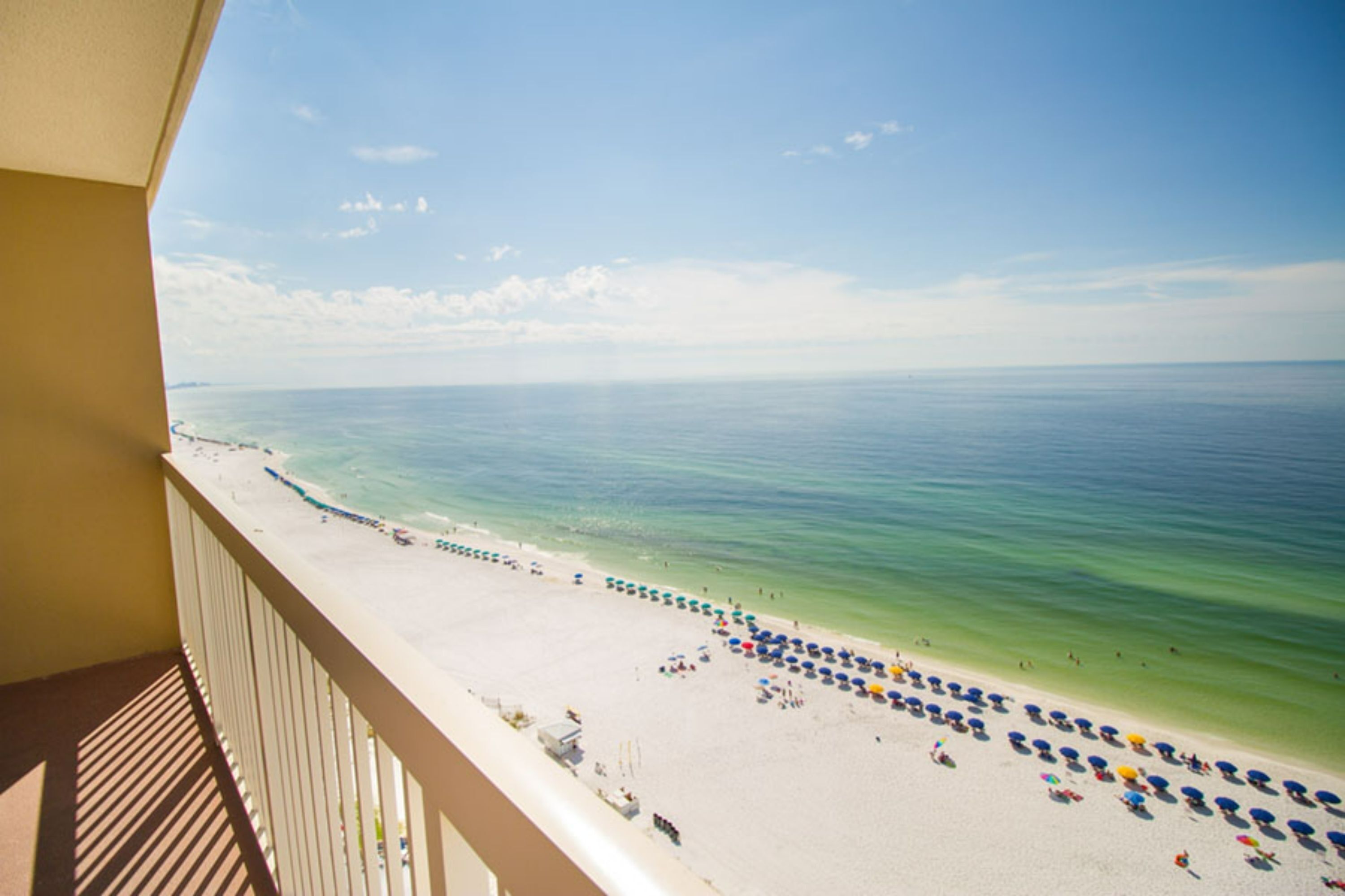Blick auf einen Strand vom Balkon aus, mit blauem Himmel, sandigem Strand und vielen Sonnenschirmen.